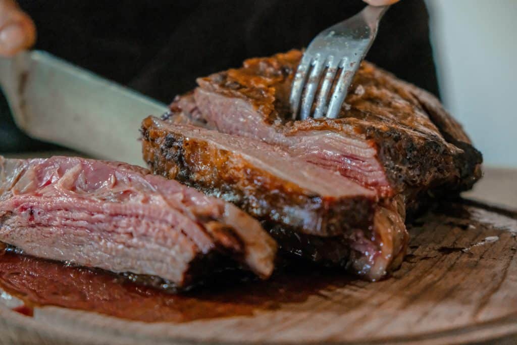 Close-up of juicy, medium-rare steak being sliced on a wooden board with a fork and knife.